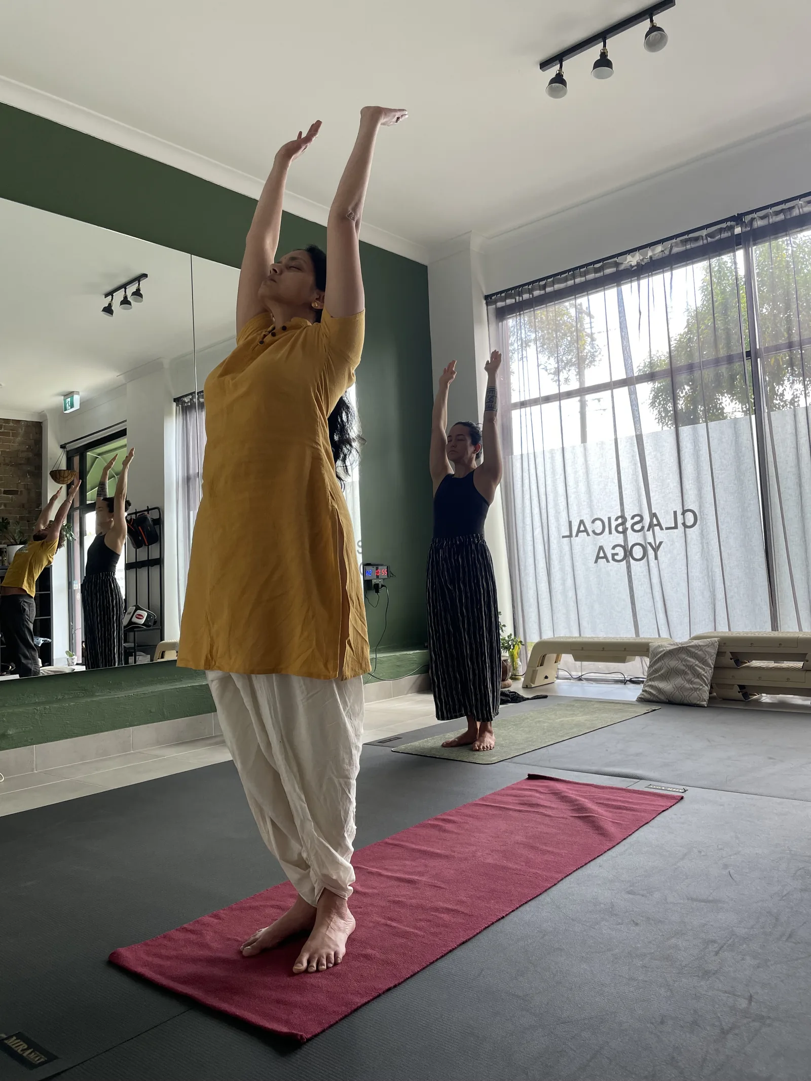 Yoga practitioner reaching both arms overhead in a sun invocation at Adiyoga in Earlwood
